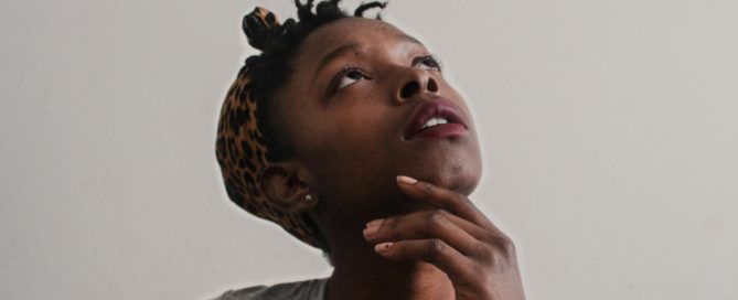 African American girl in a gray shirt looking upward in a thinking postion.